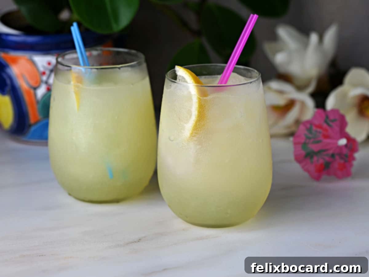 Two enticing glasses of frozen Limoncello lemonade slush, garnished with vibrant lemon slices, gleaming and ready to be enjoyed on a bright, sunny day.