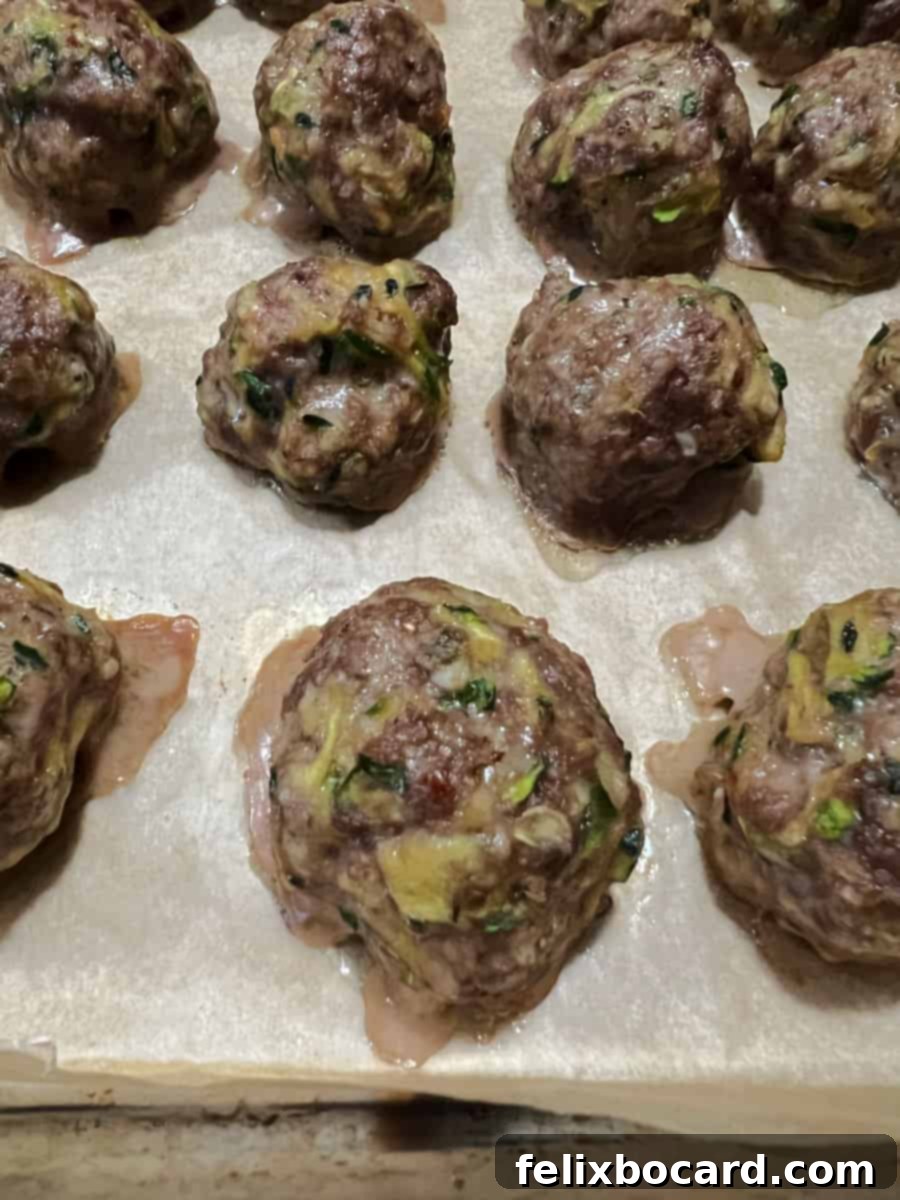 Garden Fresh Beef & Zucchini Meatballs 10 Freshly baked zucchini meatballs on a parchment-lined baking sheet, golden brown and perfectly cooked.