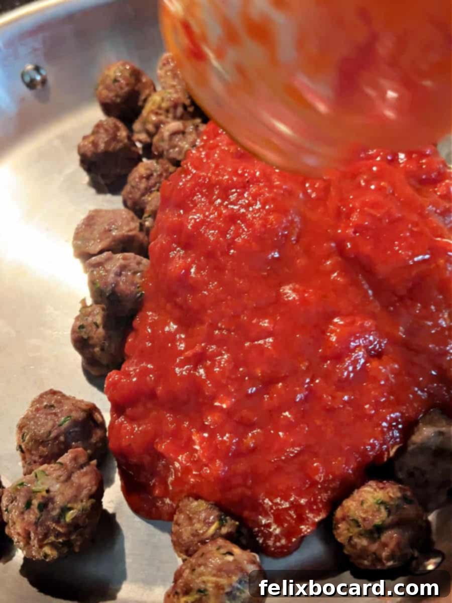 Garden Fresh Beef & Zucchini Meatballs 11 Cooked zucchini meatballs being added to a large skillet with a simmering marinara sauce.
