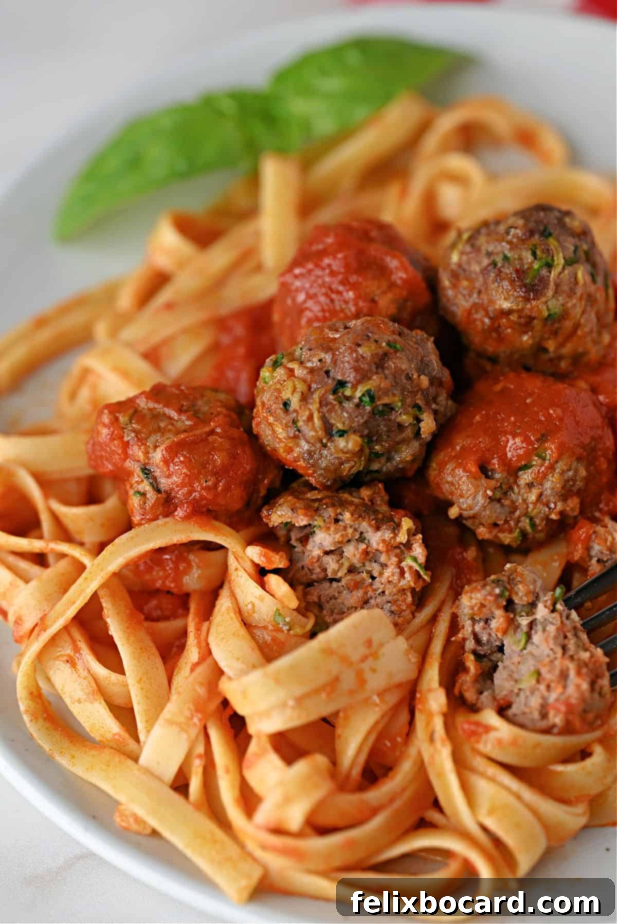 Garden Fresh Beef & Zucchini Meatballs 13 A close-up of zucchini meatballs and sauce over pasta, garnished with fresh herbs, ready to eat.