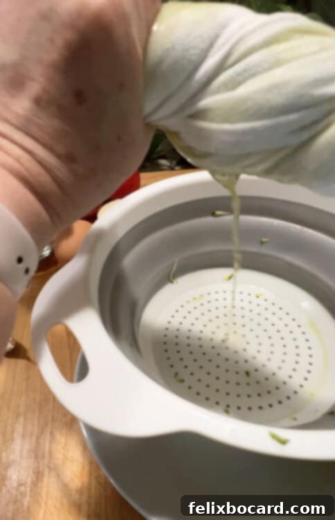 Garden Fresh Beef & Zucchini Meatballs 6 Hands twisting a kitchen towel filled with shredded zucchini, demonstrating the squeezing process to remove excess liquid.