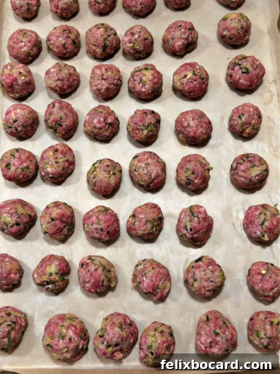 Garden Fresh Beef & Zucchini Meatballs 9 Raw zucchini meatballs arranged neatly on a parchment-lined baking sheet, ready for the oven.