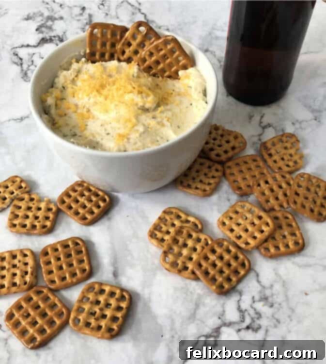 A bowl of creamy Beer Cheese Dip surrounded by a generous pile of classic twisted pretzels, perfect for dipping.