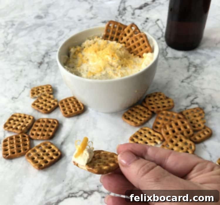 A hand holding a perfectly dipped pretzel into a bowl of creamy Beer Cheese Dip, ready to enjoy.