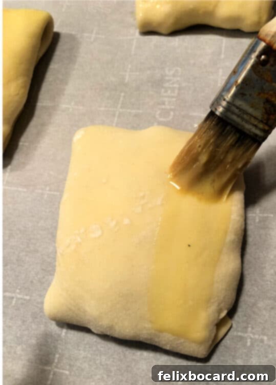 pastry on a baking sheet being brushed with egg wash