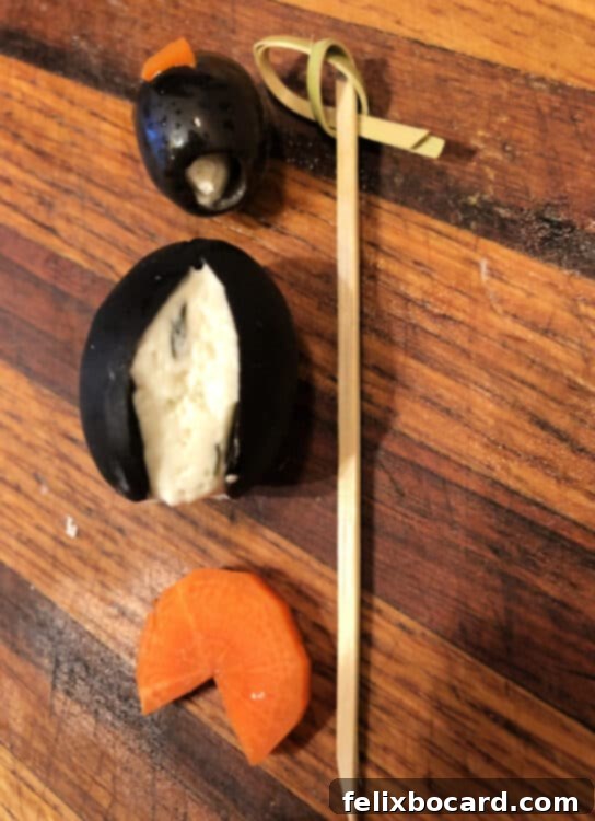 Penguin Party Bites 6 Image showcasing the assembly process of the cream cheese penguin: a small olive head and large olive body stacked on a toothpick, ready to be placed on a carrot base.