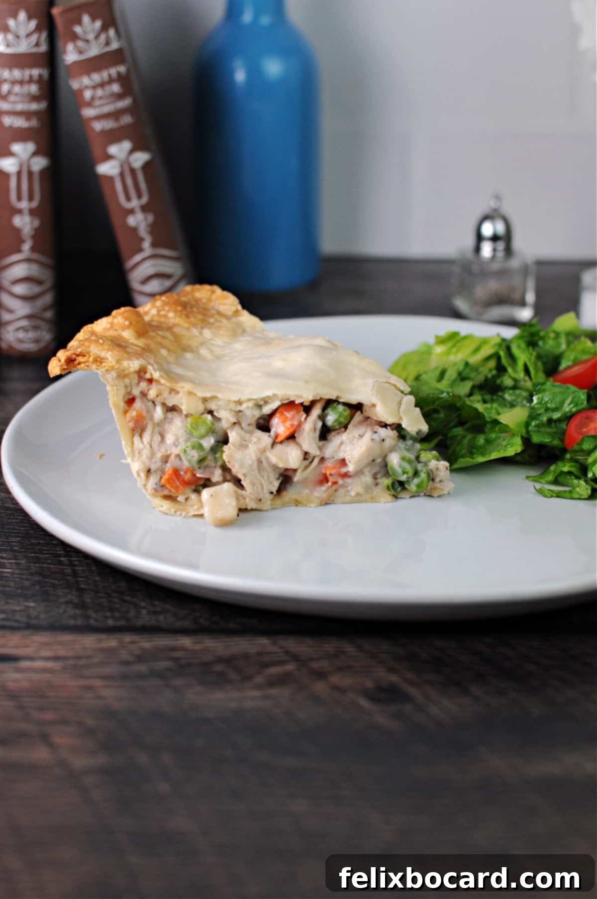 A perfectly baked slice of chicken or turkey pot pie on a white plate, accompanied by a fresh green salad.