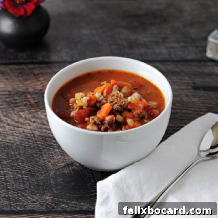 Ground Beef Barley Soup 7 White bowl of delicious barley soup, with a rustic napkin and spoon positioned beside it, ready to be enjoyed.