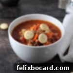 Ground Beef Barley Soup 10 White bowl of hamburger barley soup, topped with three oyster crackers