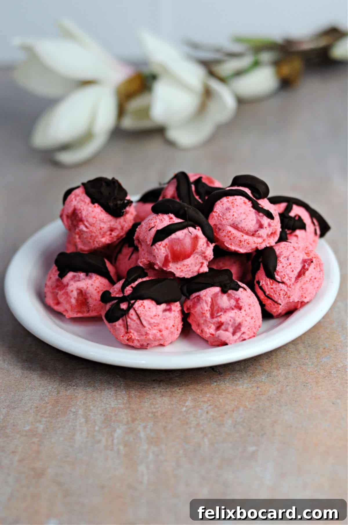 plate piled with keto strawberry bites, AKA fat bombs, drizzled with chocolate.