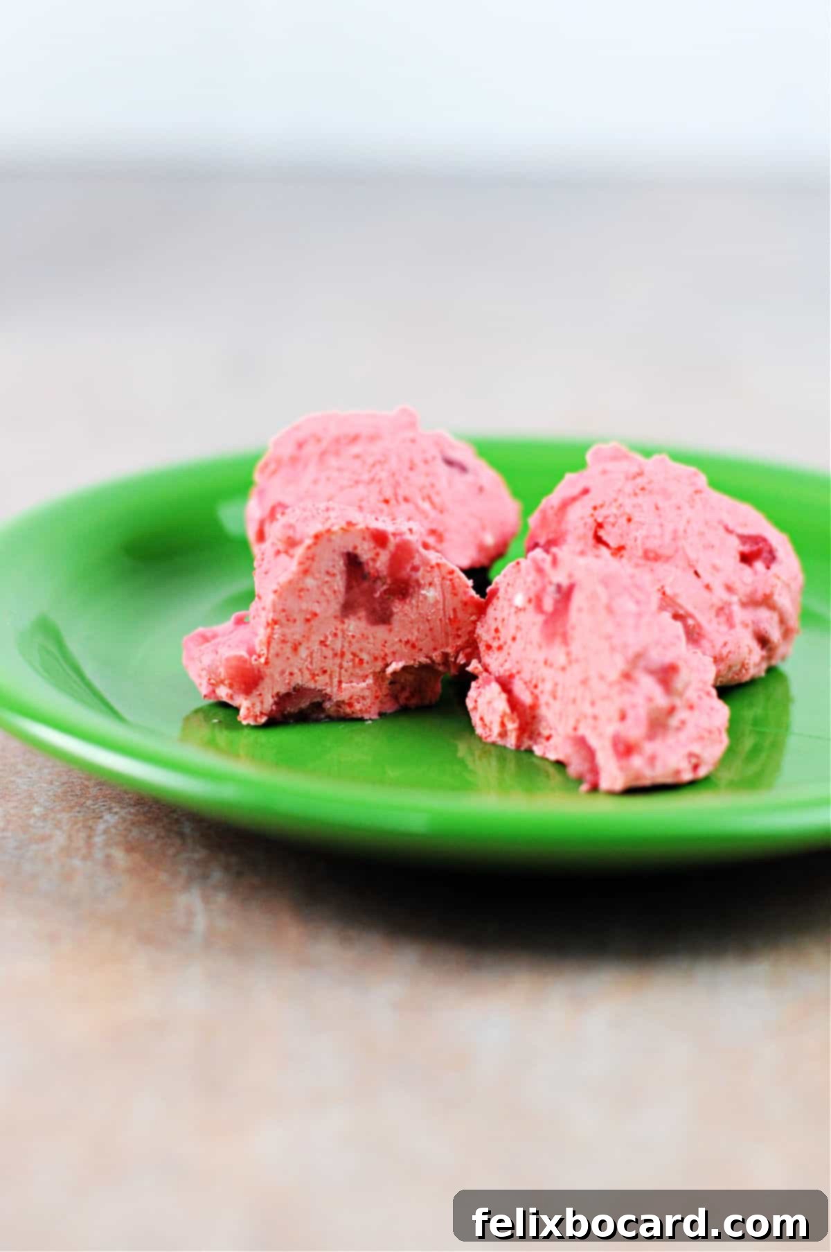 3 finished keto strawberry fat bomb snacks on a plate, one is cut open to see inside.