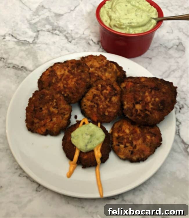 Delicious keto salmon patties served on a white plate with creamy avocado sauce.