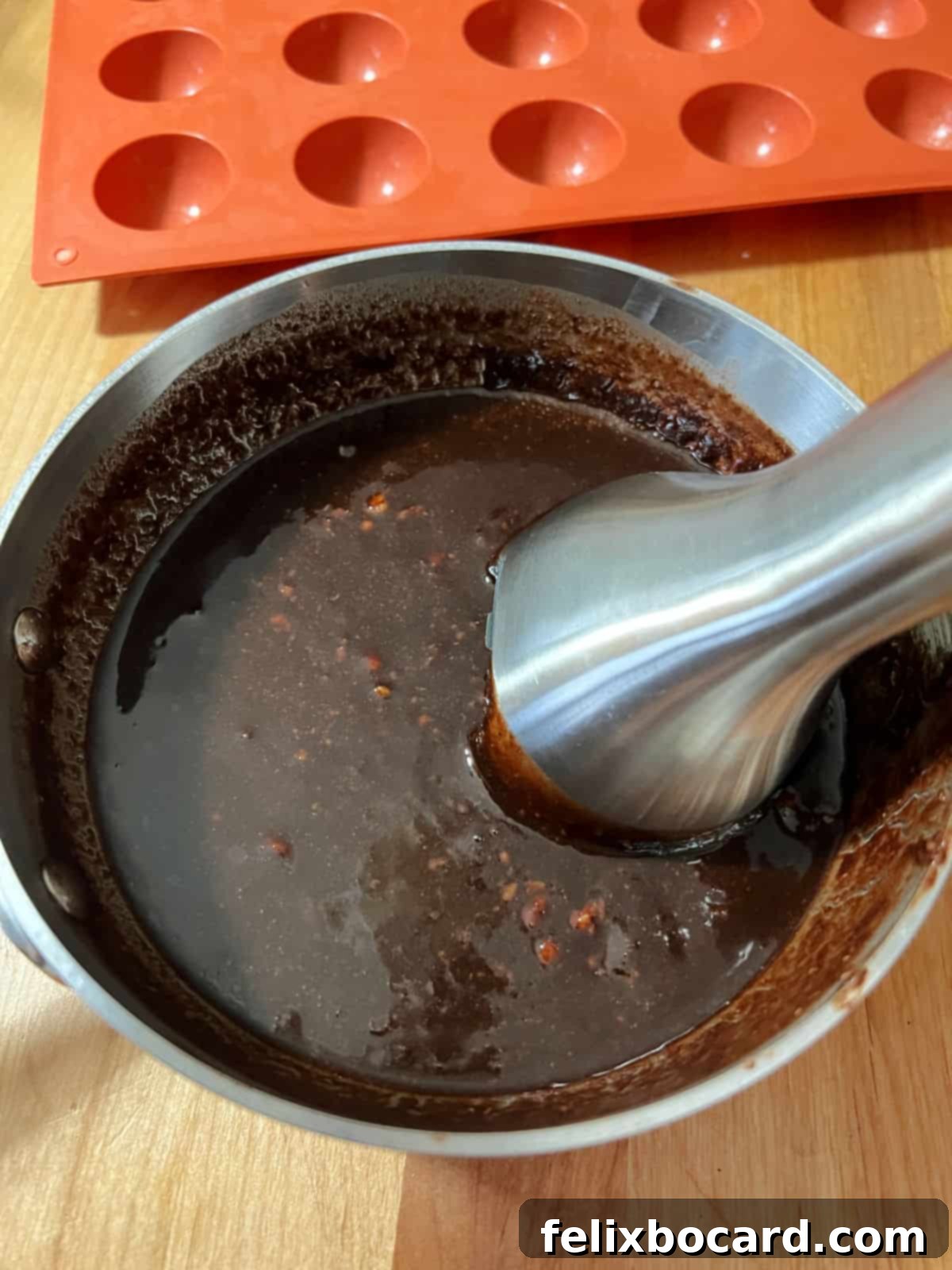 An immersion blender being used to blend the chocolate-hazelnut mixture in the saucepan until smooth and free of lumps.