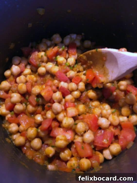 Fresh ingredients simmering in a pot for chickpea and tomato soup.