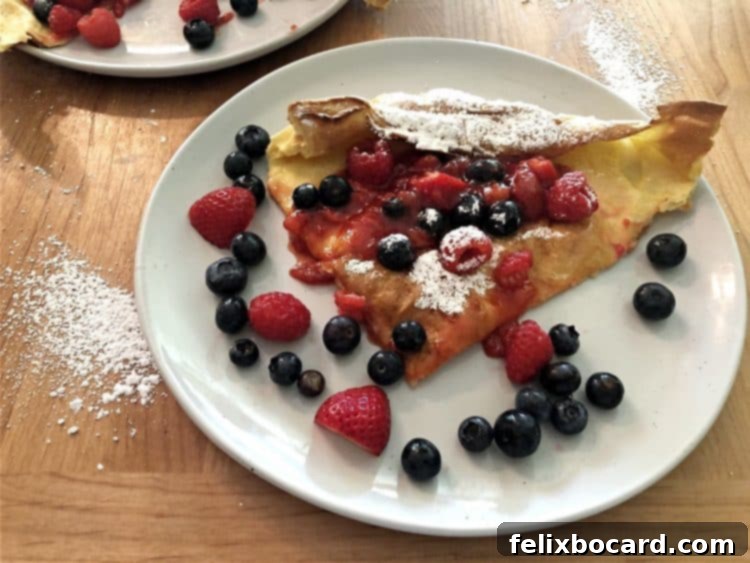 Slice of Dutch Baby with fruit and raspberry sauce