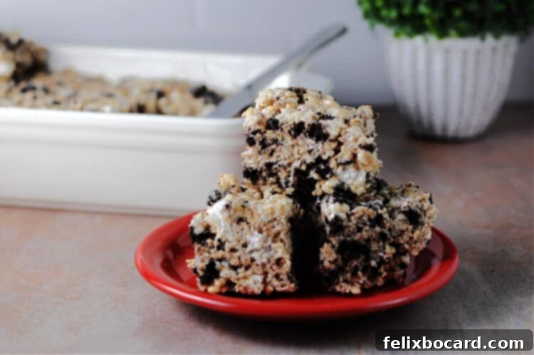 Oreo Cookies and Cream Krispie Bars 4 A stack of golden brown Oreo Krispies, adorned with visible crushed Oreo cookies, presented on a bright red plate, ready to be enjoyed.