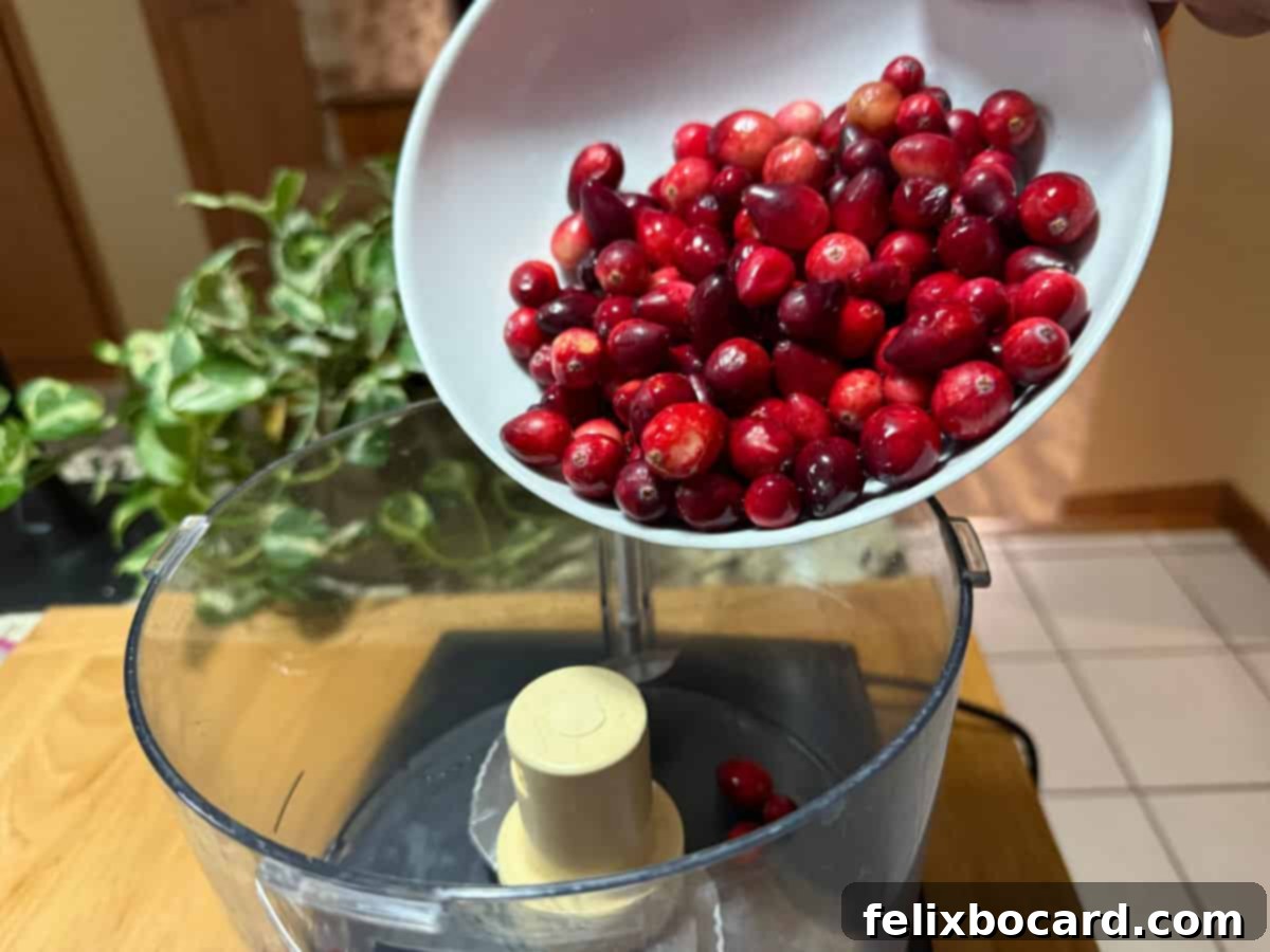 Fresh cranberries being added to a food processor bowl, ready to be minced.