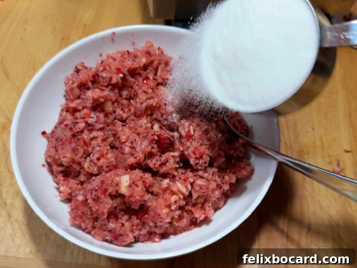 Granulated sugar being mixed into the minced cranberry and apple fruit in a bowl.