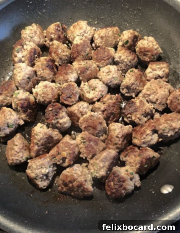 Several browned ricotta meatballs sizzling in a large non-stick skillet.