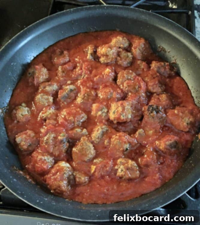 Ricotta meatballs submerged in simmering marinara sauce within a large skillet, ready to be cooked through.