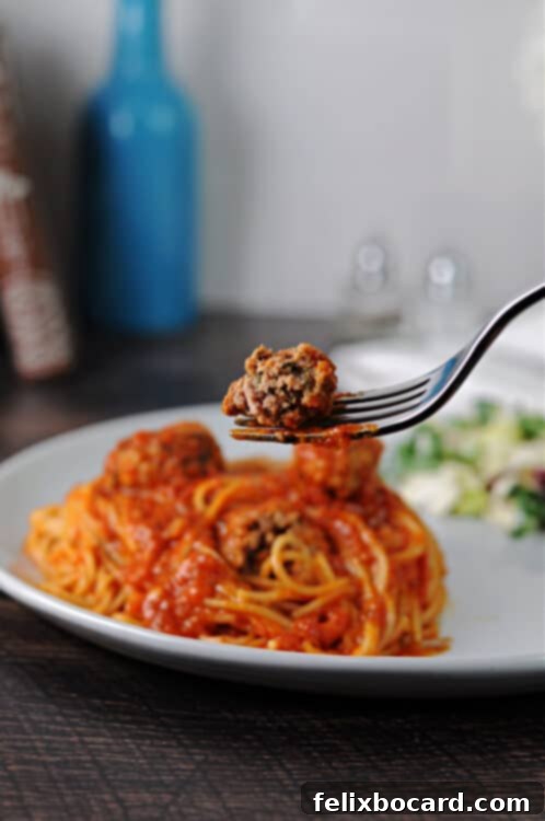 A fork holding a half-eaten ricotta meatball, suspended above a plate of spaghetti and marinara sauce.