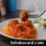 A tender ricotta meatball on a fork, poised above a plate of spaghetti with marinara sauce.