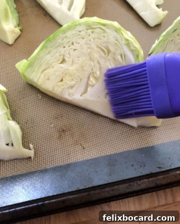 A pastry brush expertly applying olive oil to cabbage wedges on a baking sheet, ensuring even coating.