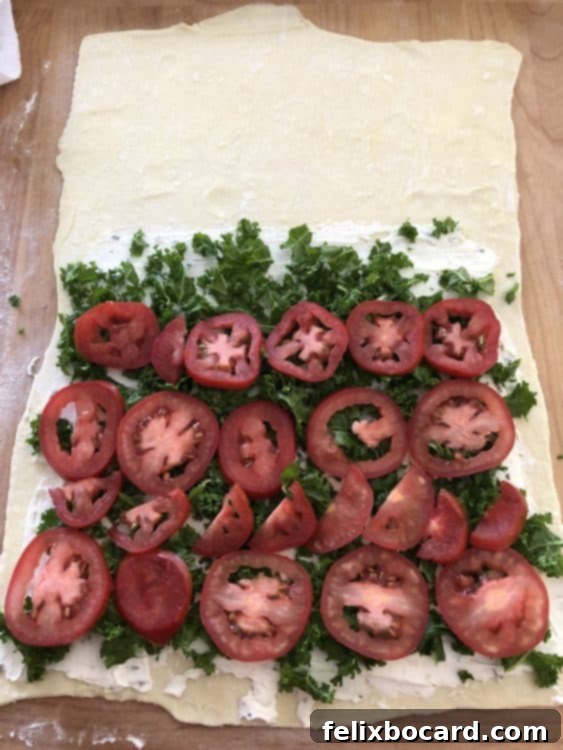 Assembling vegetarian Stromboli with cream cheese, kale, and tomatoes