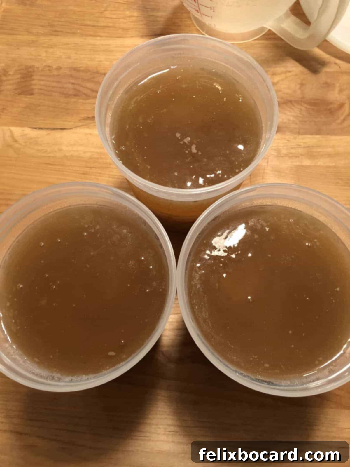 Three jars of golden, homemade bone broth cooling on a counter, ready for storage.