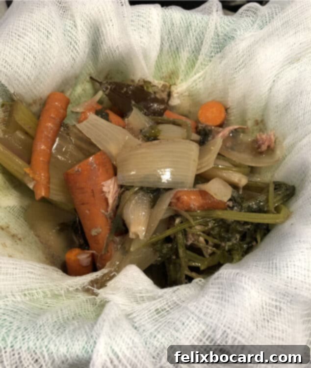 Cooked bones and vegetables in a cheesecloth-lined colander, ready for straining to separate solids from liquid.