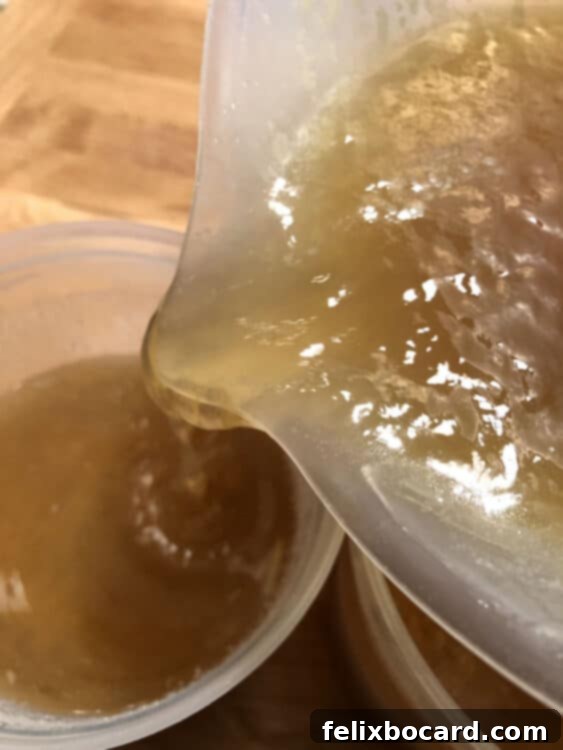Gelatinous bone broth being poured from a jar, showcasing its rich, thick consistency.