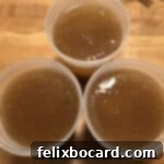 Three jars of golden bone broth, a top-down view showing the rich color and gelatinous quality, ready for freezing.