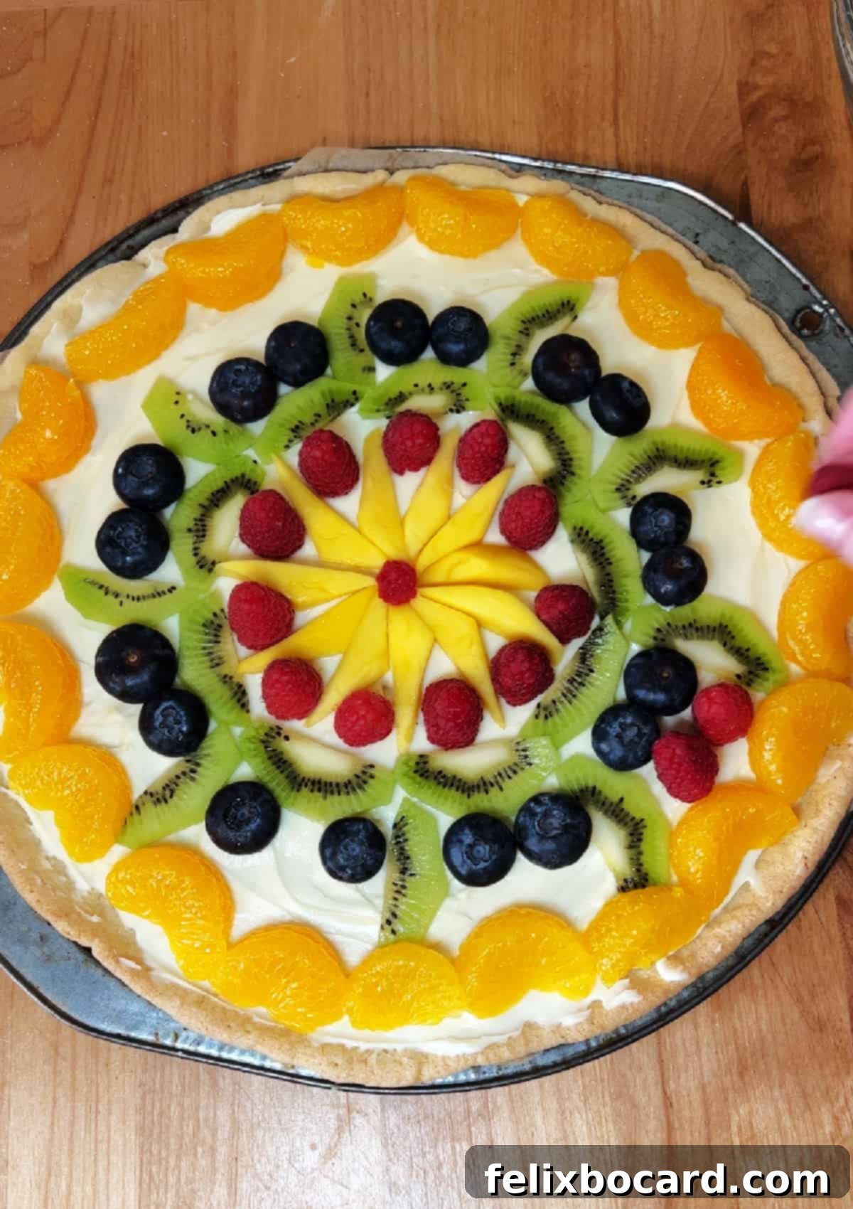 Decorating the fruit pizza with an arrangement of berries, kiwi, and mandarin oranges.