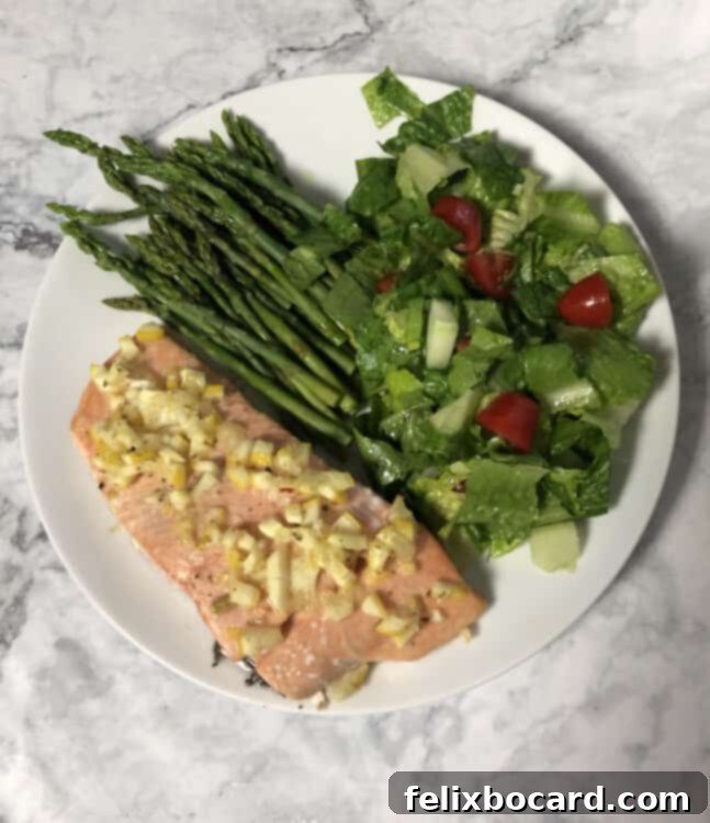 Top-down view of baked salmon generously topped with whole lemon dressing, served alongside a fresh green salad and tender asparagus.