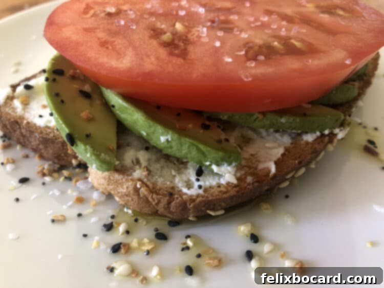 13 Creative Avocado Toast Recipes 8 A close-up of avocado toast with a thick, ripe tomato slice, ready to be enjoyed as a refreshing meal.