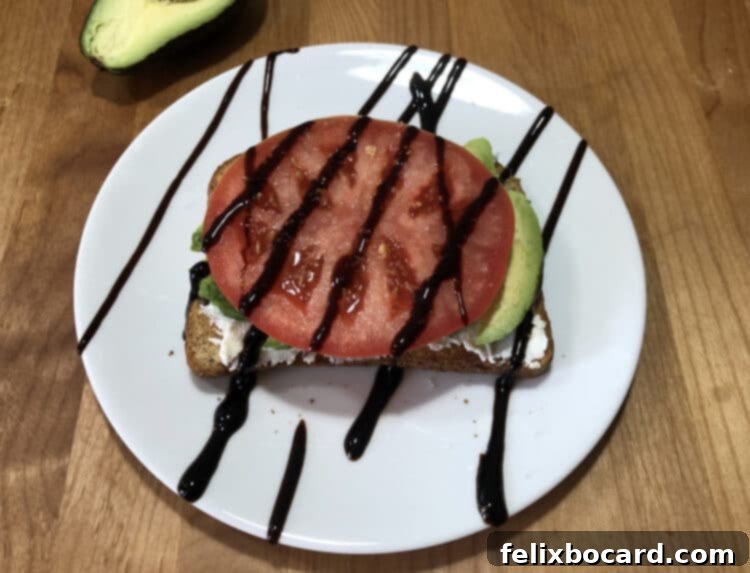 13 Creative Avocado Toast Recipes 9 Avocado toast elegantly topped with a layer of ricotta, fresh avocado, a vibrant tomato slice, and a rich balsamic glaze drizzle.
