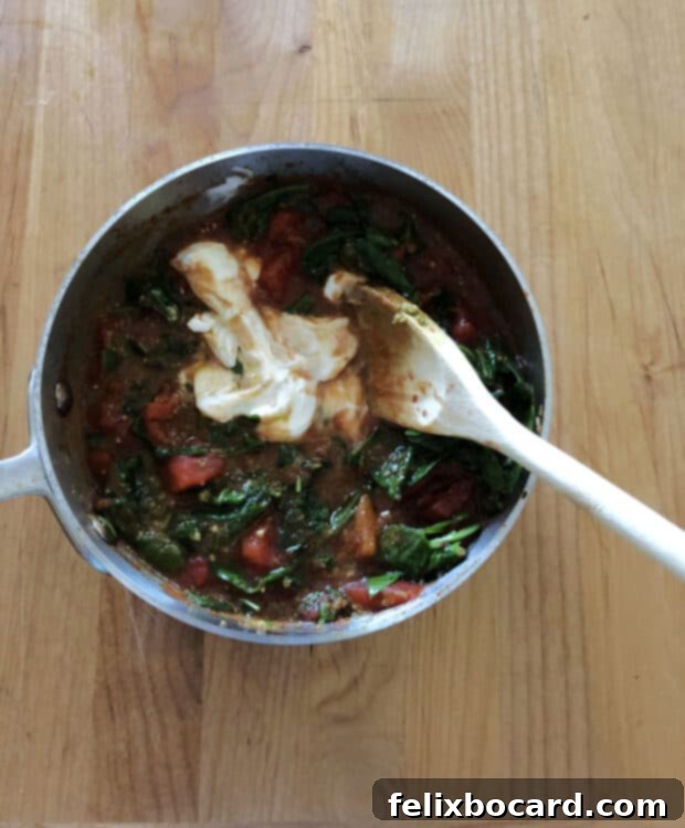 Sour cream being gently folded into the warm tomato and pesto sauce, creating a smooth and creamy texture.