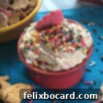 Dunkaroo Dip, also known as funfetti cake batter dip, in a small bowl garnished with sprinkles and surrounded by crackers and cookies for dipping