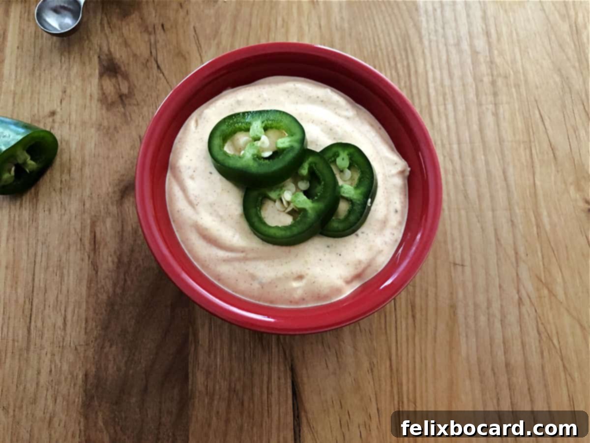 Copycat Taco Bell Creamy Jalapeno Quesadilla Sauce 2 Small red bowl with creamy quesadilla sauce garnished with fresh jalapeño slices, ready to be enjoyed.