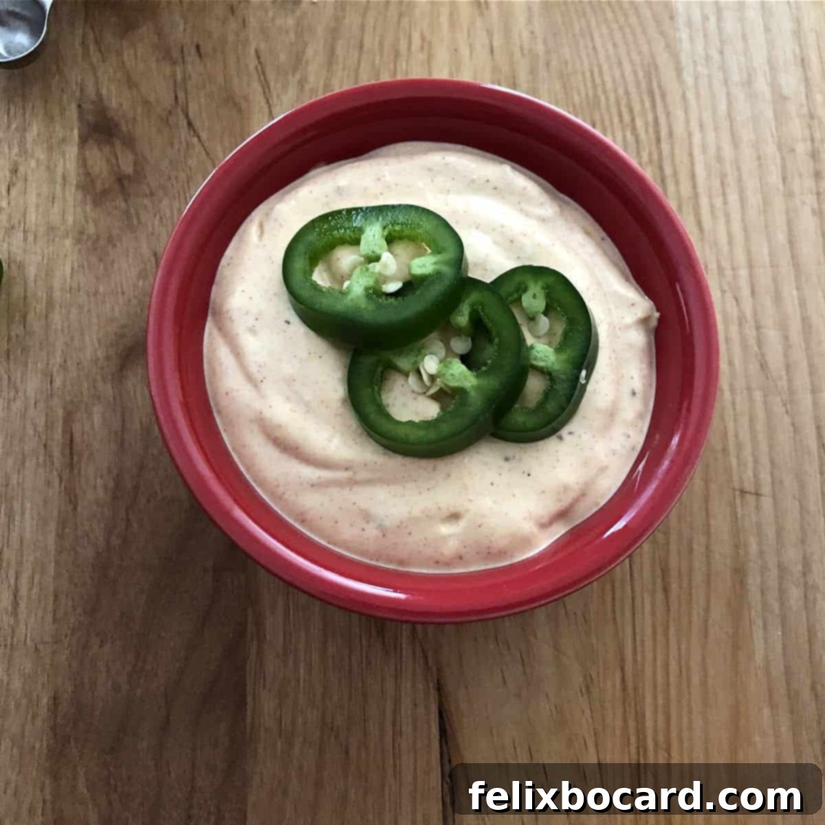 Copycat Taco Bell Creamy Jalapeno Quesadilla Sauce 5 Vibrant red bowl filled with homemade Taco Bell quesadilla sauce, garnished with thinly sliced jalapeños.