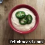 Copycat Taco Bell Creamy Jalapeno Quesadilla Sauce 7 Homemade Taco Bell quesadilla sauce in a red bowl, garnished with sliced jalapenos on top.