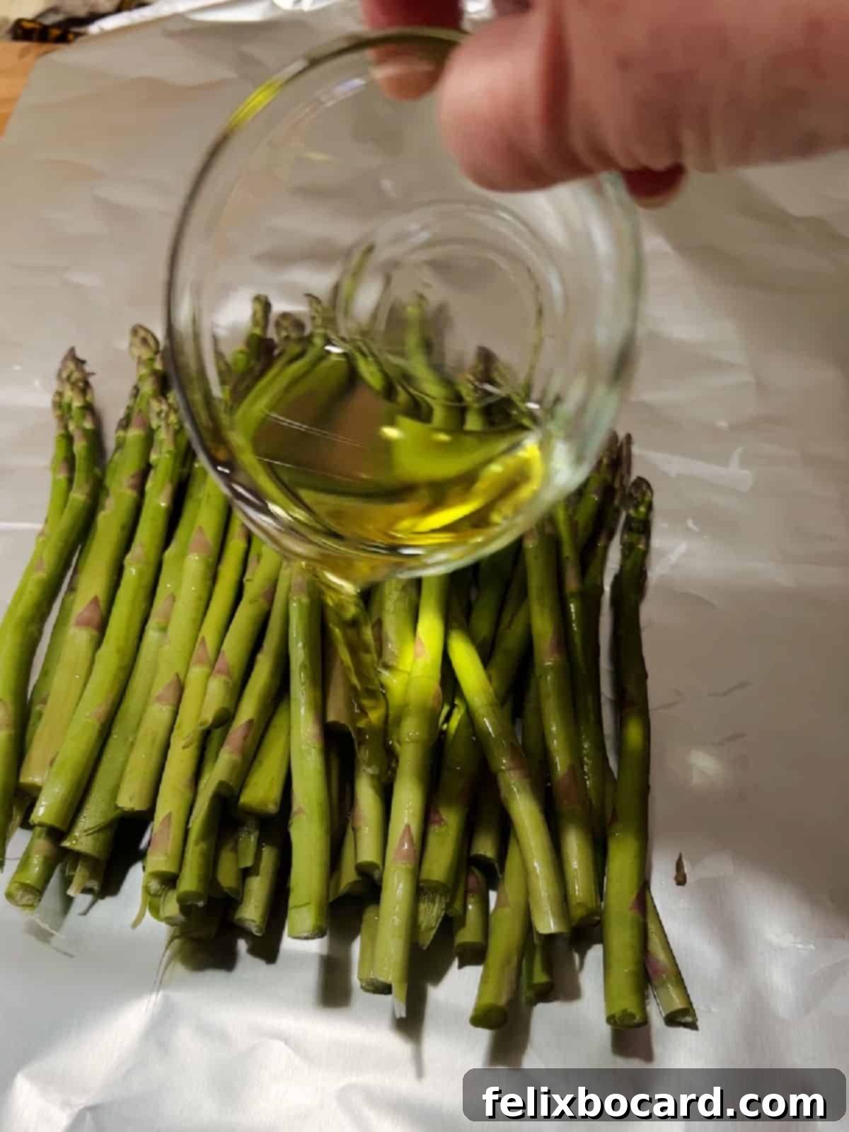 Oil drizzling on asparagus sitting on foil sheet.