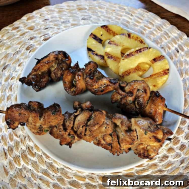 2 chicken skewers on a white plate with some grilled pineapple slices