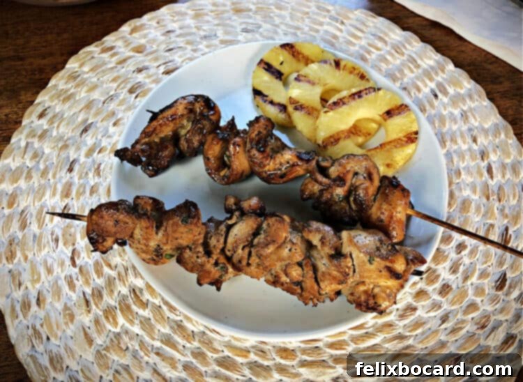 chinese chicken on a stick served on a white plate with grilled pineapple