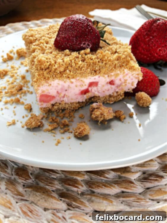 A perfectly square slice of frozen strawberry dessert on a small white plate, showing the distinct layers of graham cracker crust and creamy pink filling.