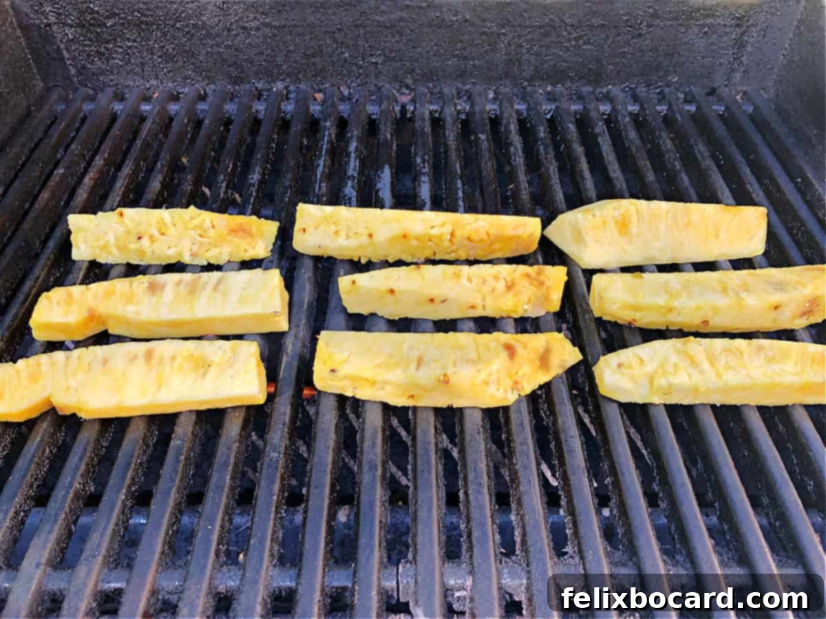 Sweet and Smoky Grilled Pineapple 5 Pineapple spears cooking on the grill, showing distinct grill marks.