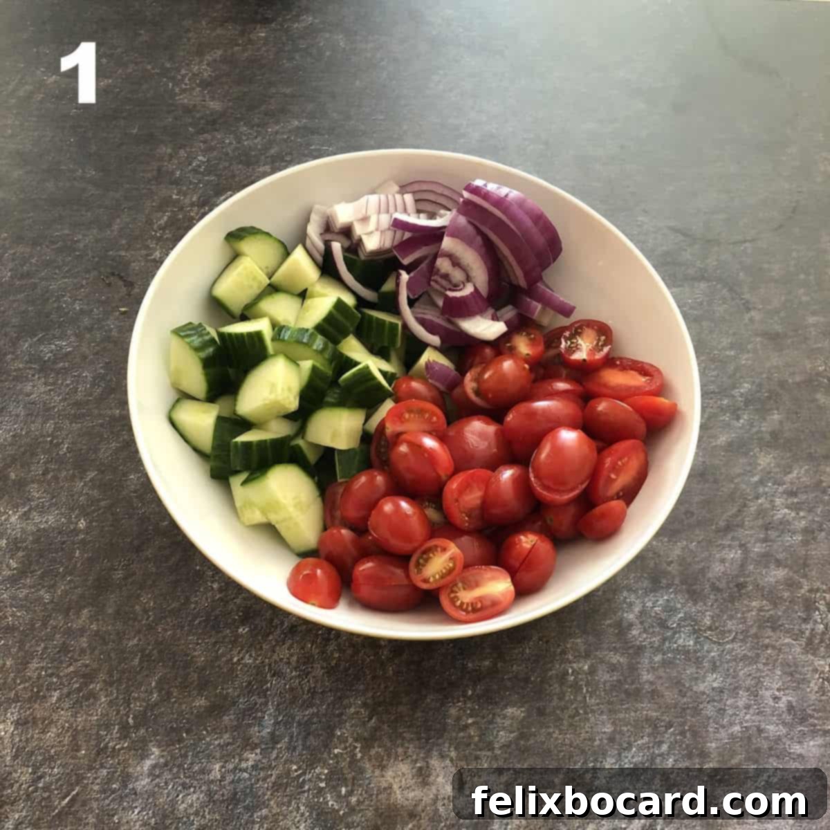 Freshly chopped cucumbers, halved grape tomatoes, and thinly sliced red onions waiting in a large mixing bowl.
