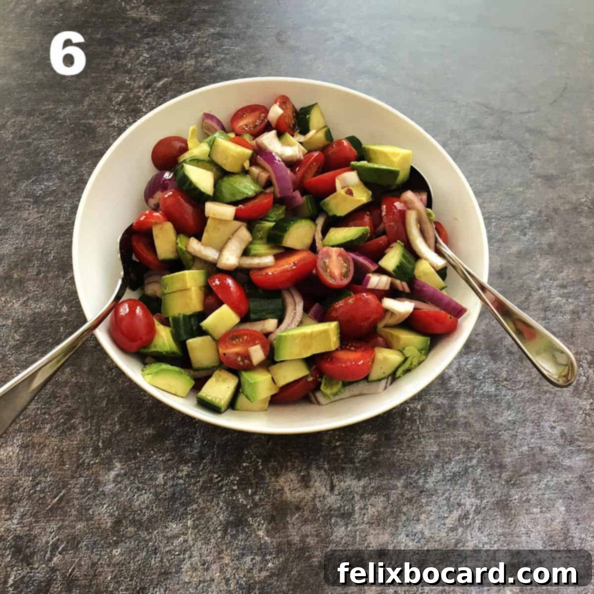 The finished balsamic cucumber tomato salad, fully mixed with avocado, ready to be served in a large white bowl.