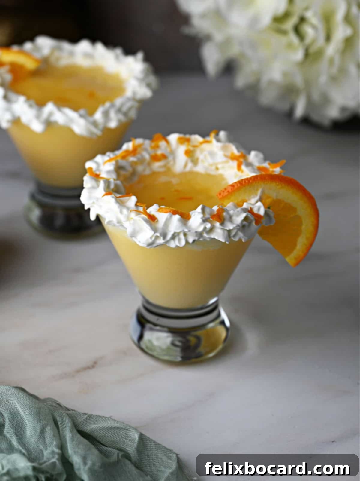 Two vibrant Orange Creamsicle Cocktails, garnished beautifully with a swirl of whipped cream, delicate orange zest, and a fresh orange slice, set against a bright background.
