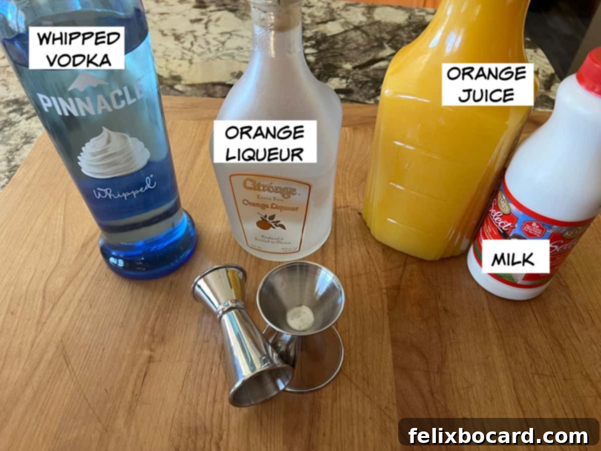 A flat lay photograph showcasing the key ingredients for an Orange Creamsicle Cocktail: a bottle of whipped vodka, a bottle of orange liqueur (Triple Sec), a glass of fresh orange juice, and a carton of milk.